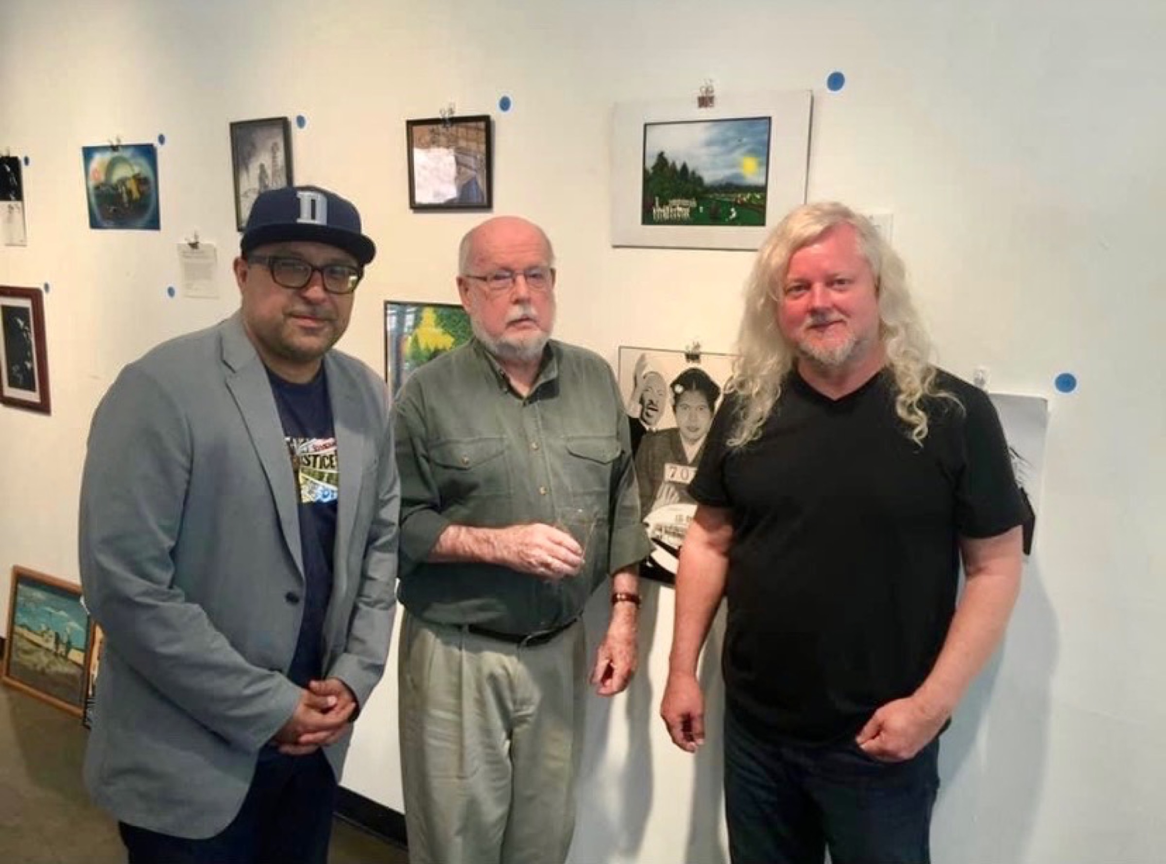 Murray Smither (center) at a gallery exhibition with two attendees, works hung on the surrounding walls.