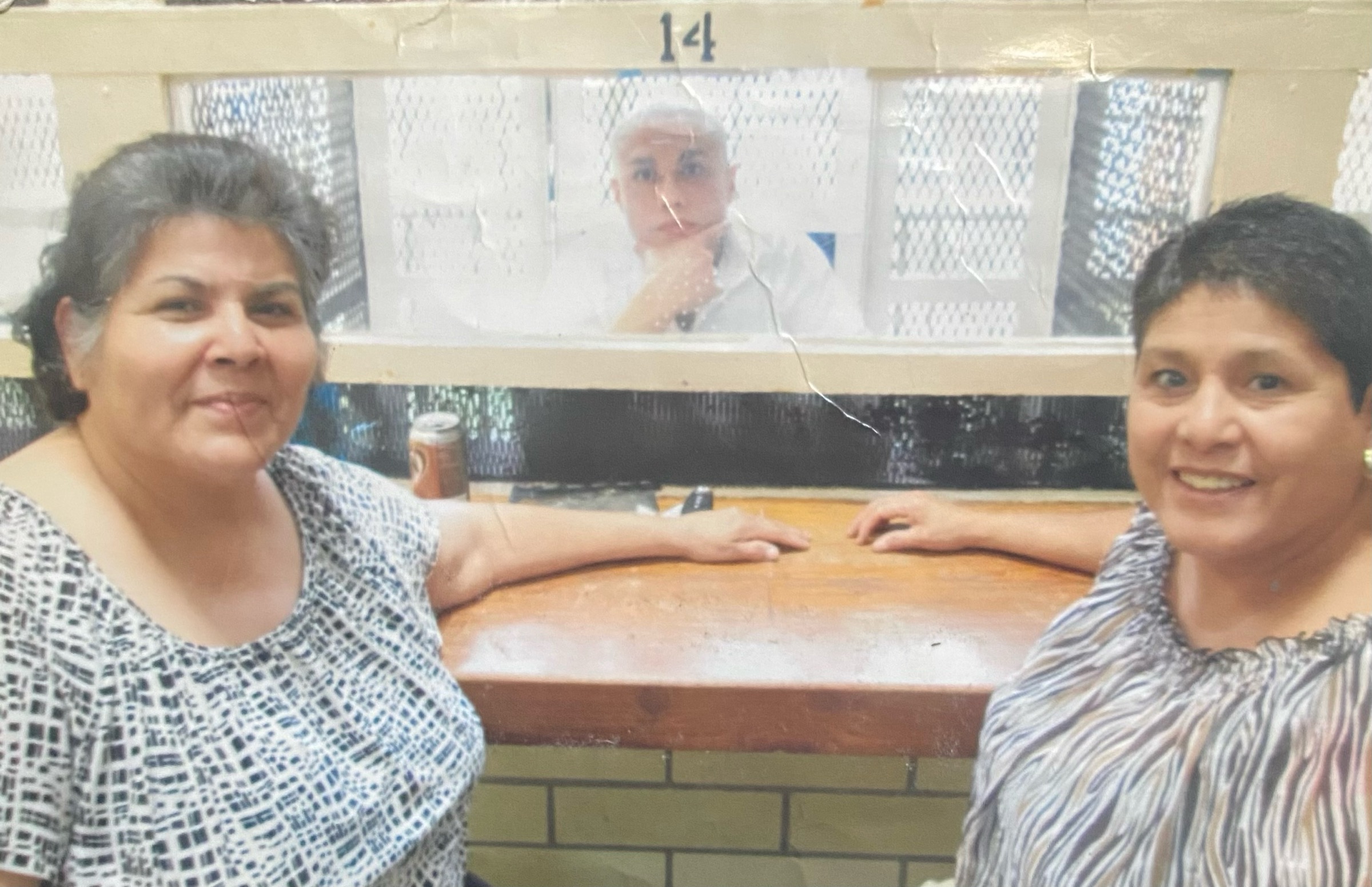 Daniel seated behind the visitation partition while two members of his family sit at the counter, acting as intermediary.